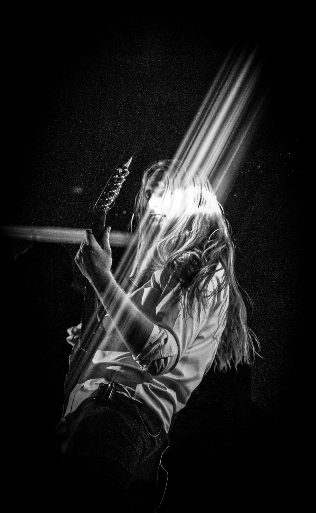 Guitarist with long hair caught in a beam of stage light, black and white