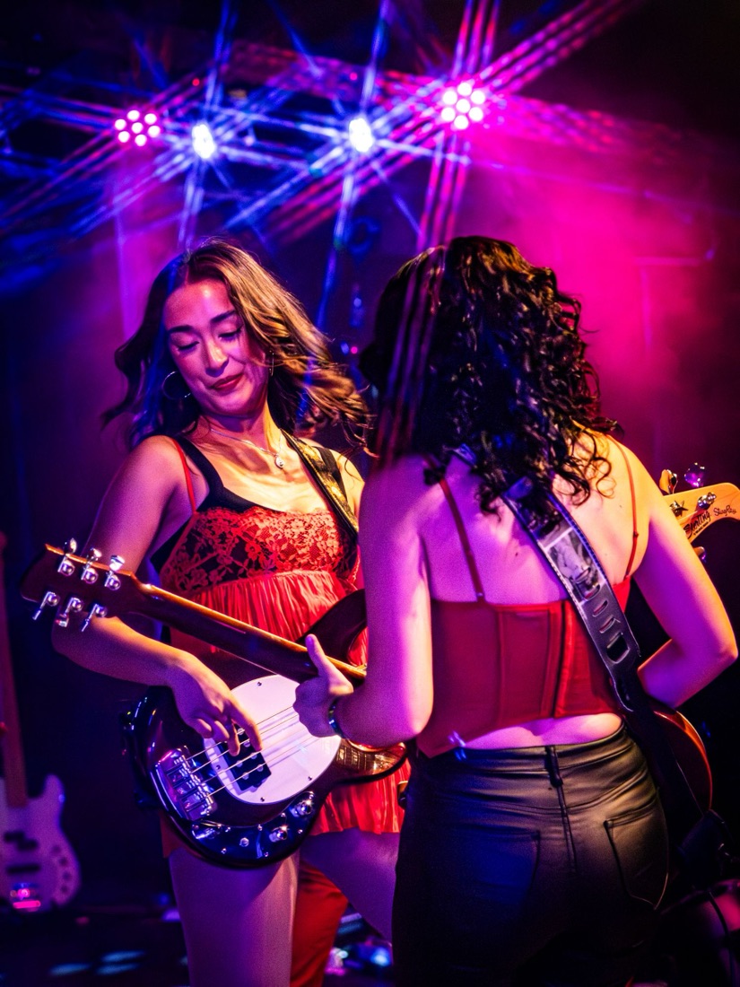 Bassist and guitarist in red playing face to face under pink and blue lights