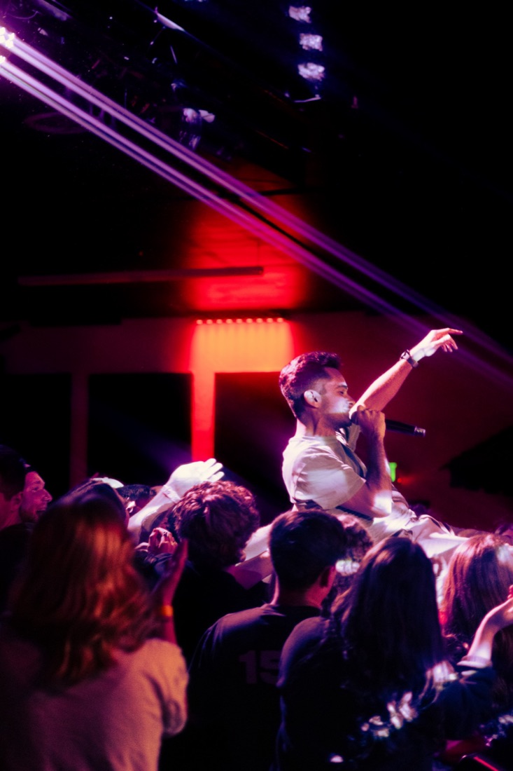 Vocalist crowd surfing with a microphone under red and purple light