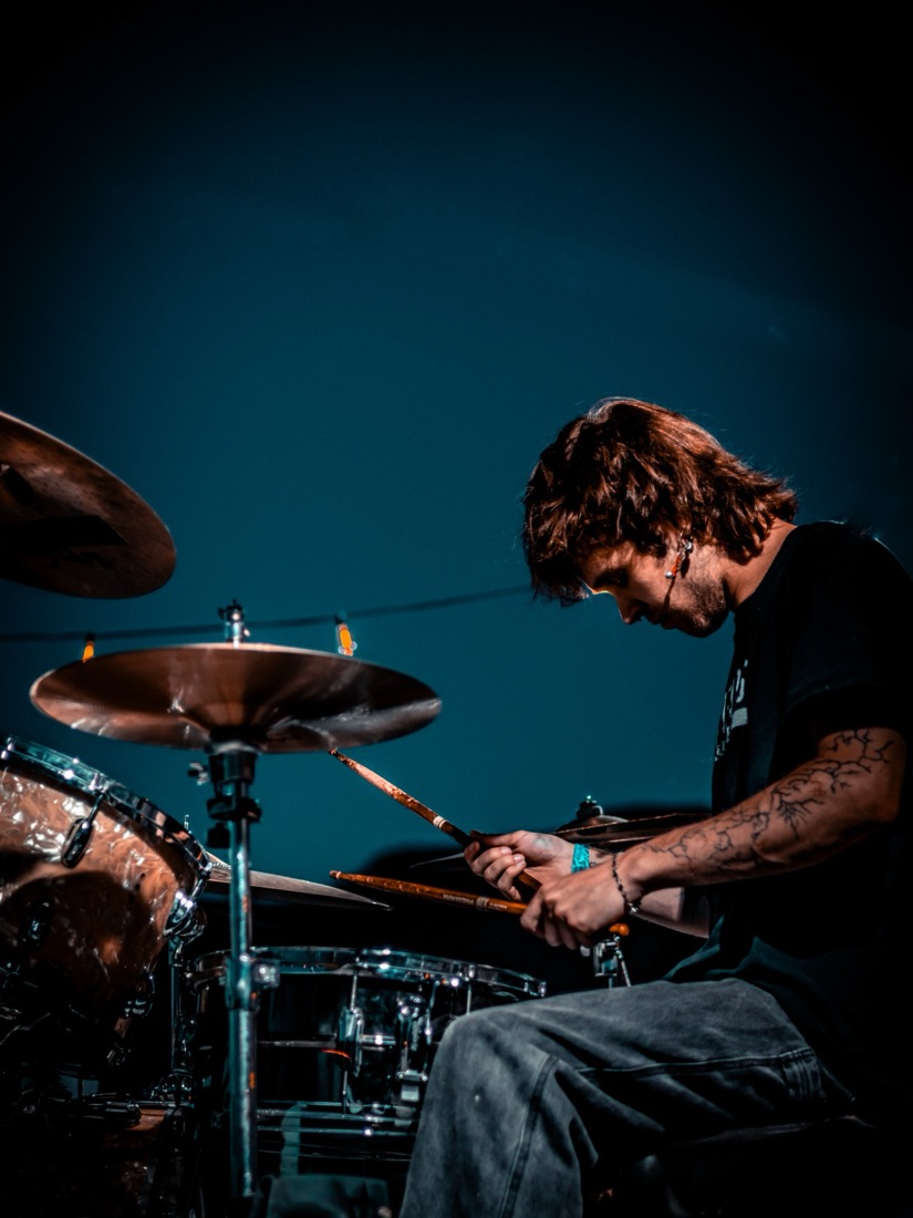 Drummer with a tattooed arm against a deep teal background
