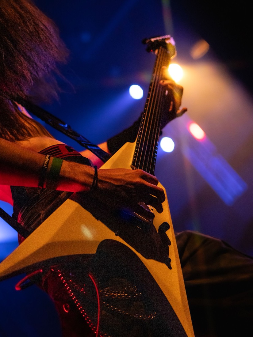 Close-up of a yellow flying V guitar with blue stage lights behind
