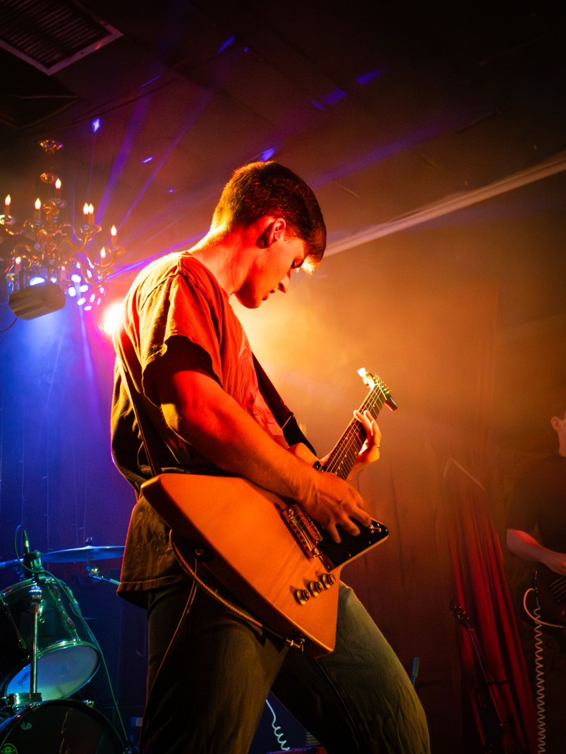Guitarist with an Explorer guitar under a chandelier and orange haze