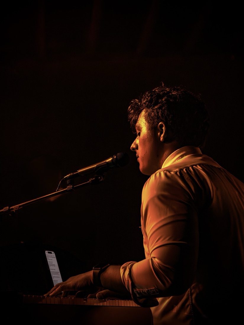 Singer at a keyboard in a single amber light