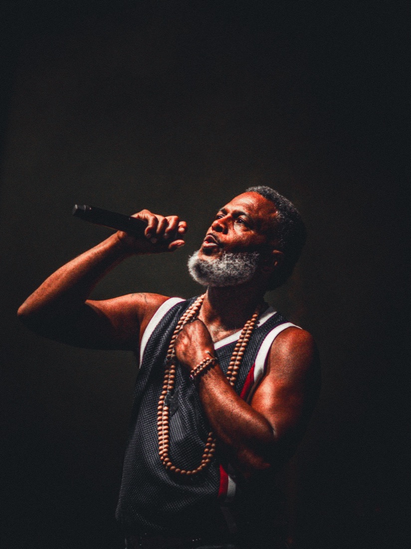 Gray-bearded vocalist singing upward in a single spotlight