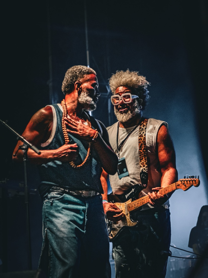 Vocalist and guitarist in white glasses sharing a laugh on stage